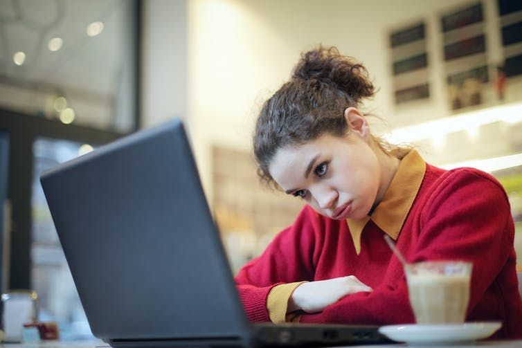 Female student wearing a red jumper and yellow shirt looking at her laptop with a frustrated expression