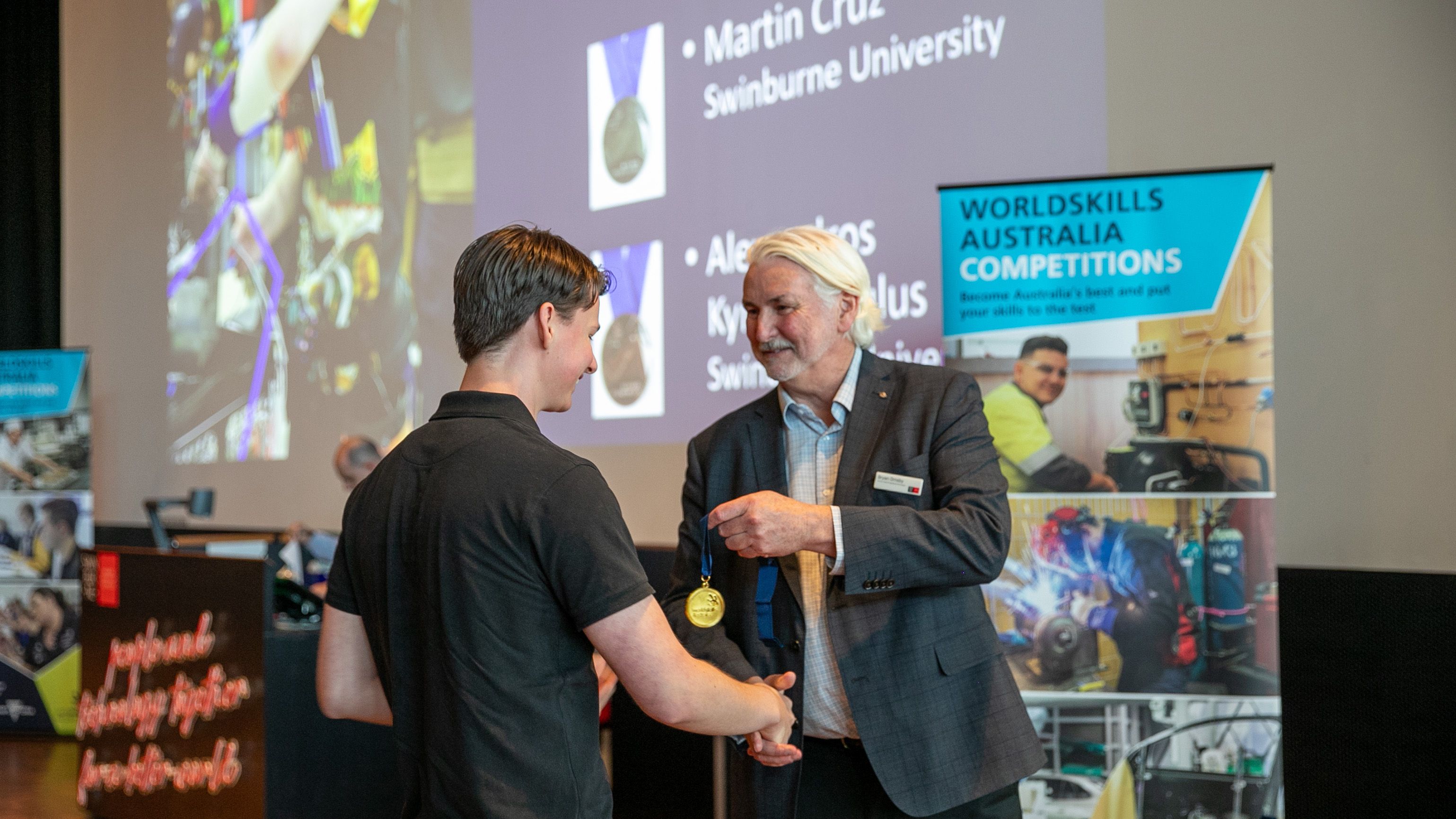 A man in a suit hands a medal to a person while shaking hands