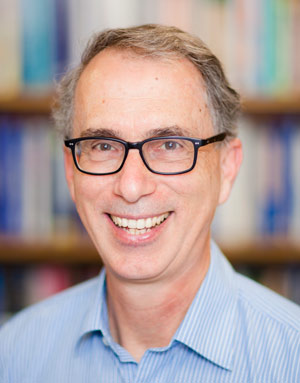 Image of David Karoly smiling wearing a blue shirt and black glasses.