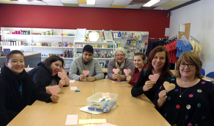 A group of students and teachers sitting around a table holding hand-made paper hearts.