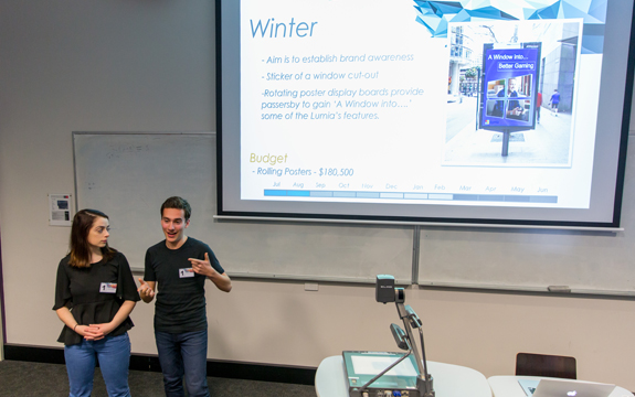 Advertising students stand at the front of a lecture theatre presenting with a powerpoint 