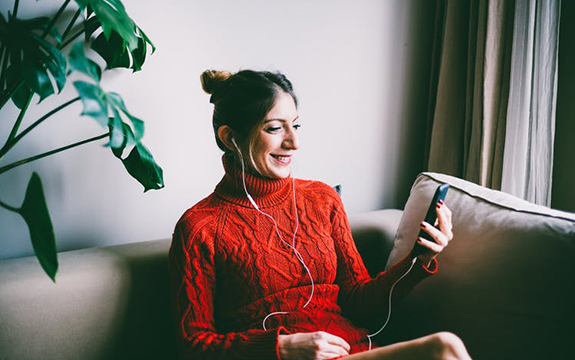 Woman using a smartphone and earbuds to make a phone call from a sofa