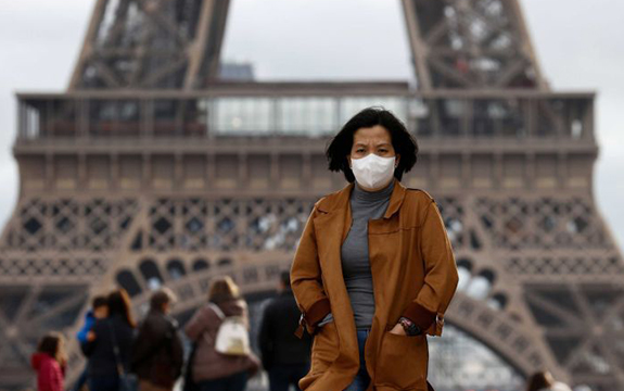Woman standing in front of the Eiffel Tower wearing a face mask