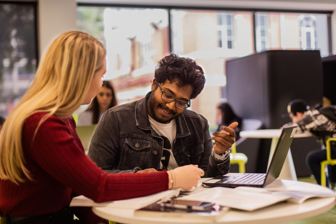 Female student discusses study with male student with laptop at the Swinburne library