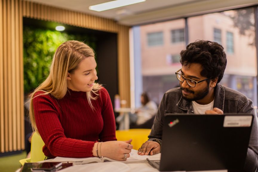 Two people sitting in front of a laptop talking 