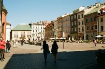 A shadow of two people enjoying a drink walking through an old European town square surrounded by old buildings.