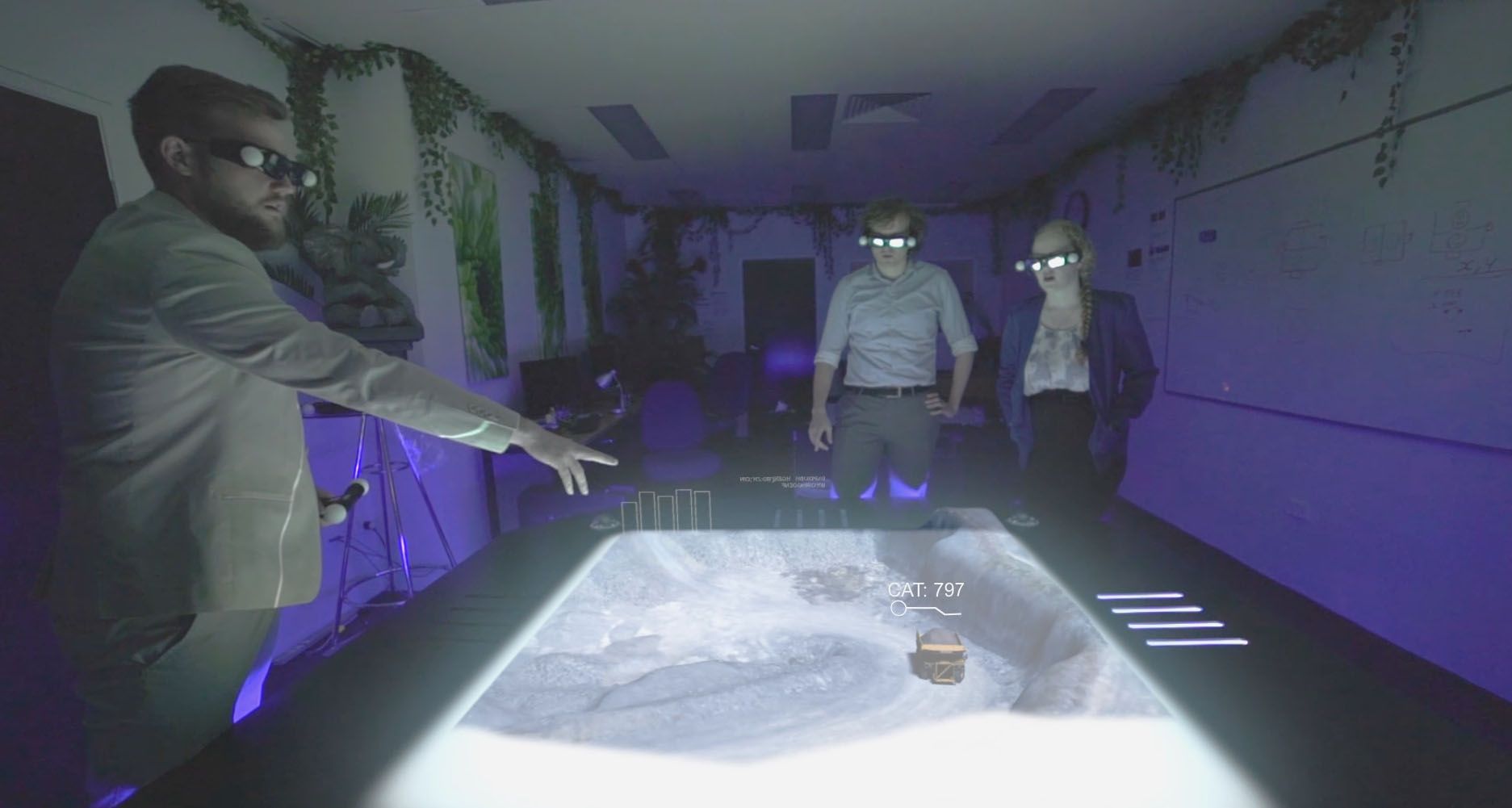 Two people with 3D glasses and wands stand around a holgram table projecting a 3D image of a city