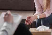 Close-up of woman's hands during counseling meeting with a professional therapist. Box of tissues and a hand of counselor blurred in the front.