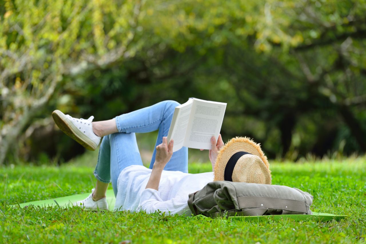 Woman lying on green grass reading a book