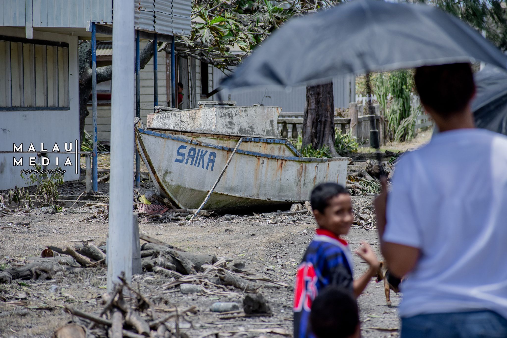 Two Tongans observing damage caused by the Tsunami in January 2022 a small child and an adult holding an umbrella
