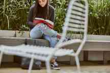 Student sits on bench reading a book with chair in the foreground
