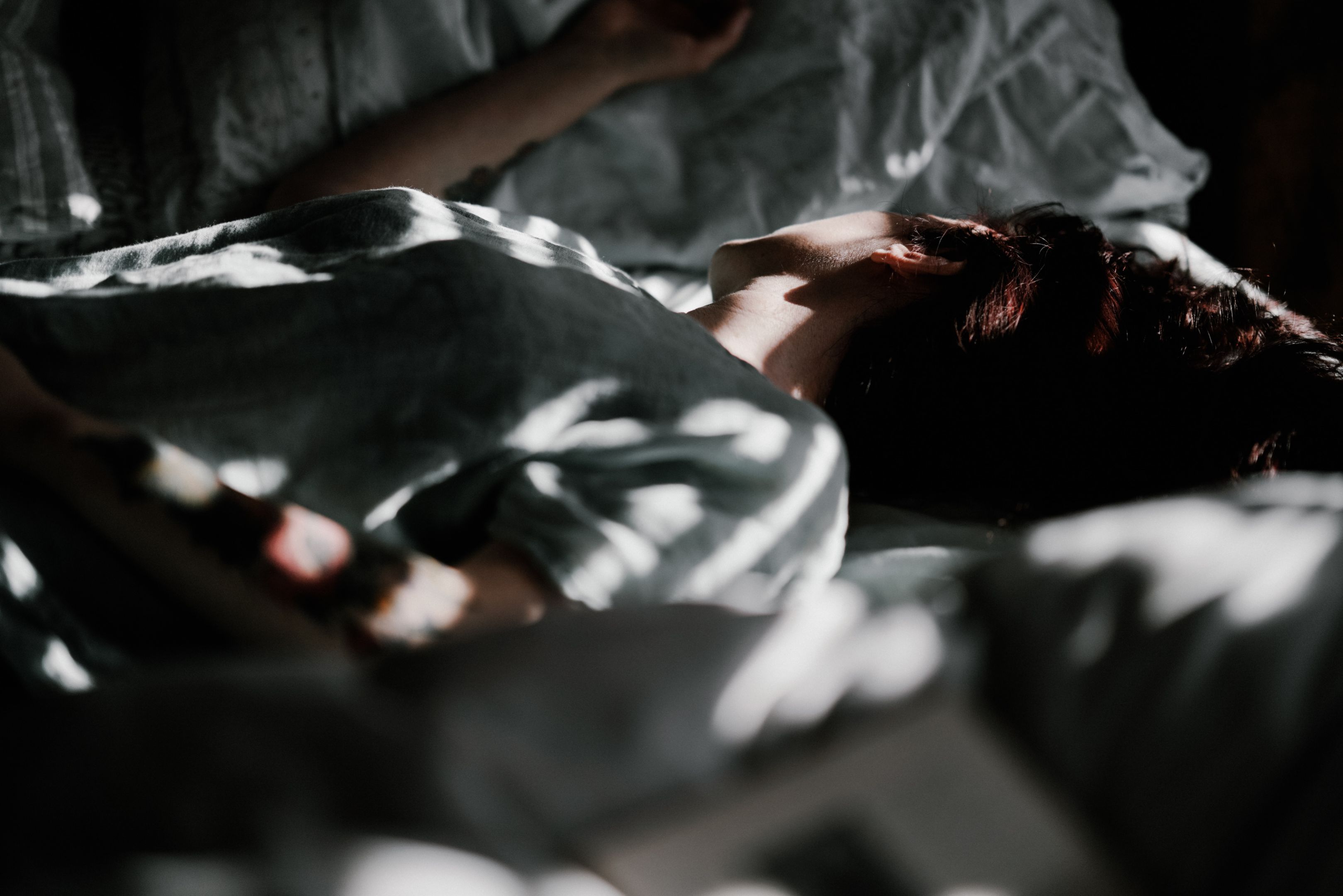 Person sleeping in bed, dappled sunlight filters through