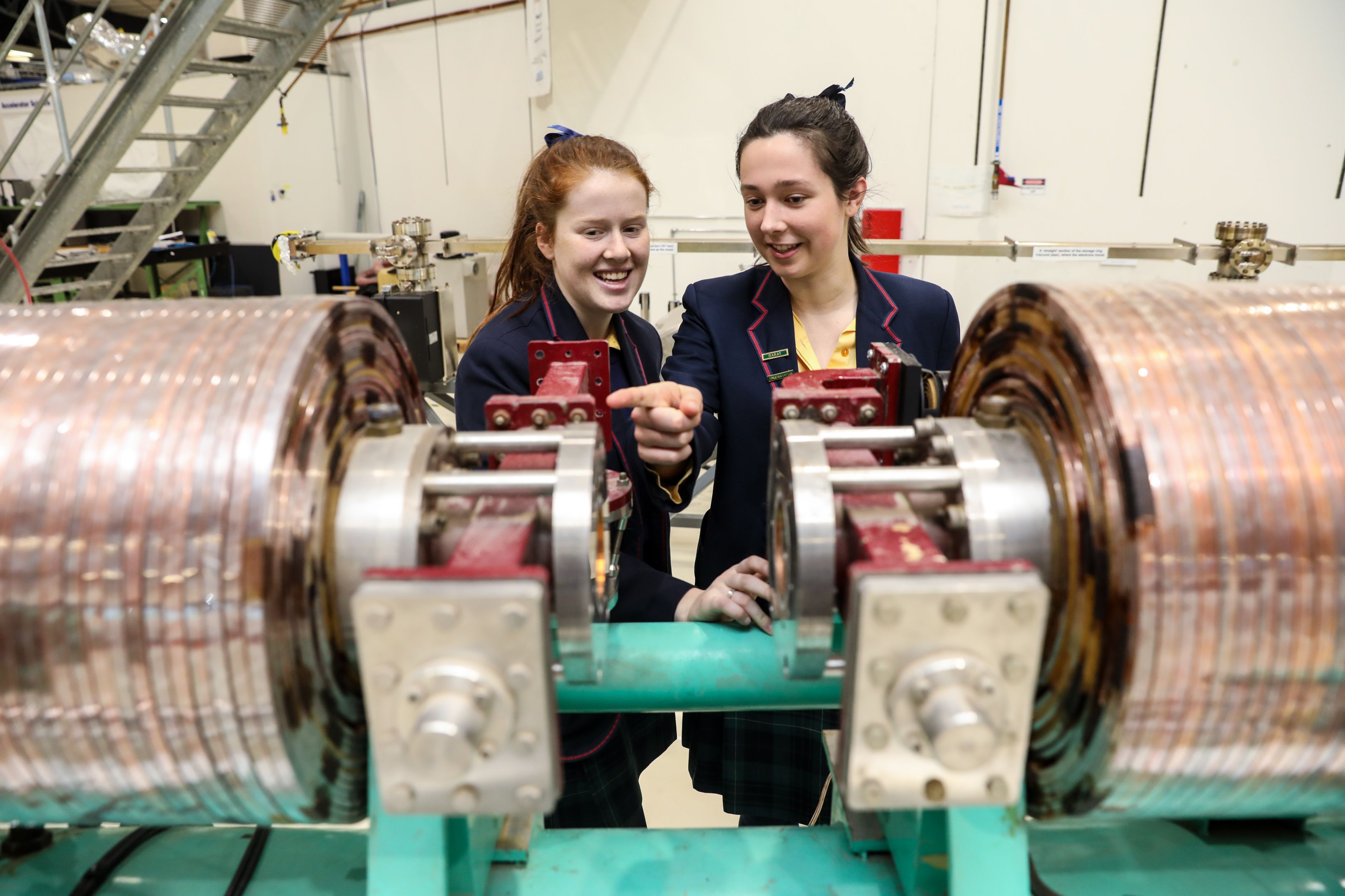 Two smiling female high school students inspecting a synchrotron machine