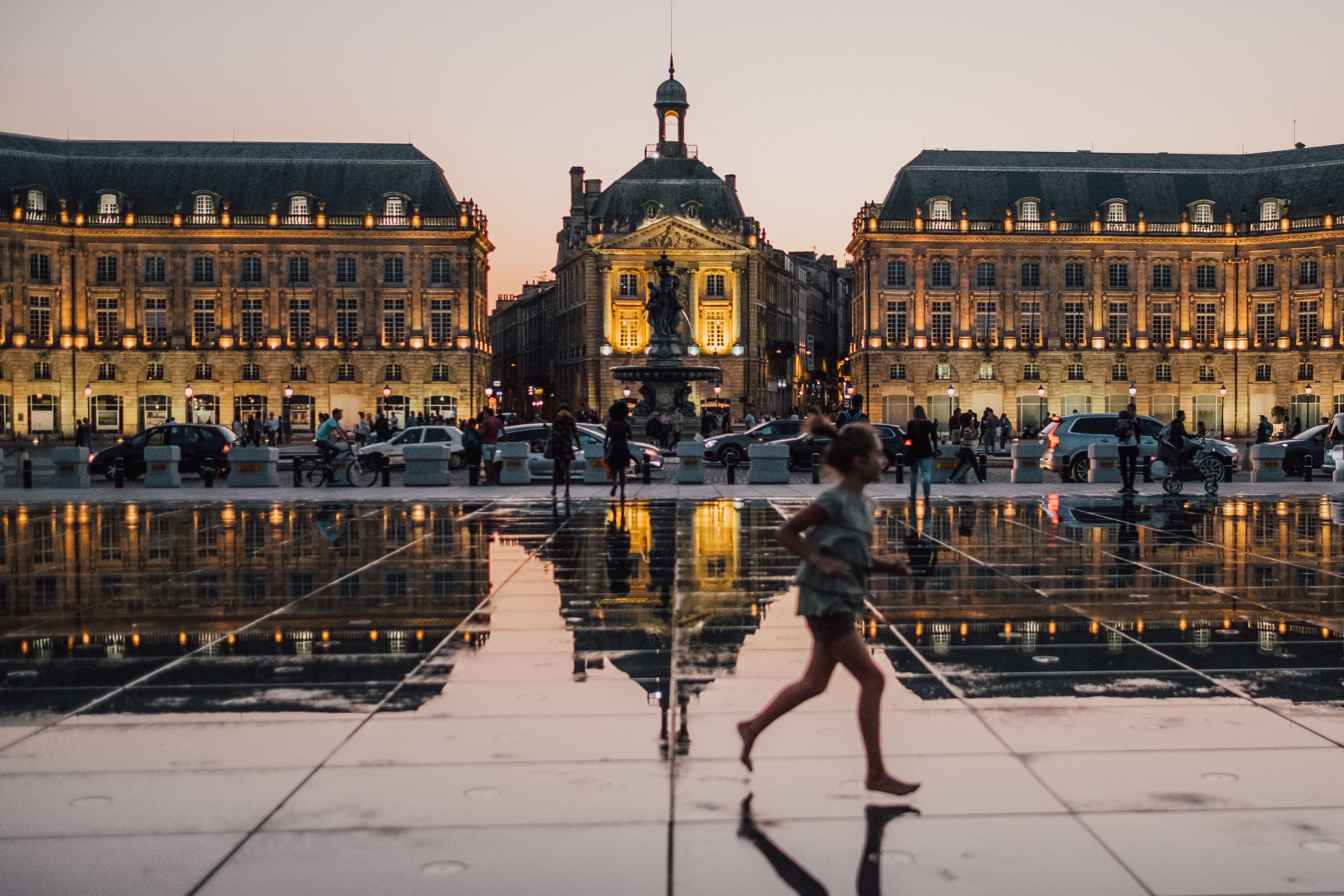 Image of lit up buildings in the city of Bordeaux in France. It is night time and the floor is showing a beautiful mirror image of the buildings.