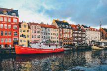 Image of colourful houses and a red boat along a river called Nyhavn in Copenhagen, Denmark.