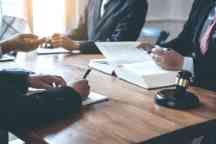 Four business lawyers in suits working together at a meeting table with a legal book and gavel.