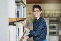 landscape woman glasses standing by bookshelf in library during the day
