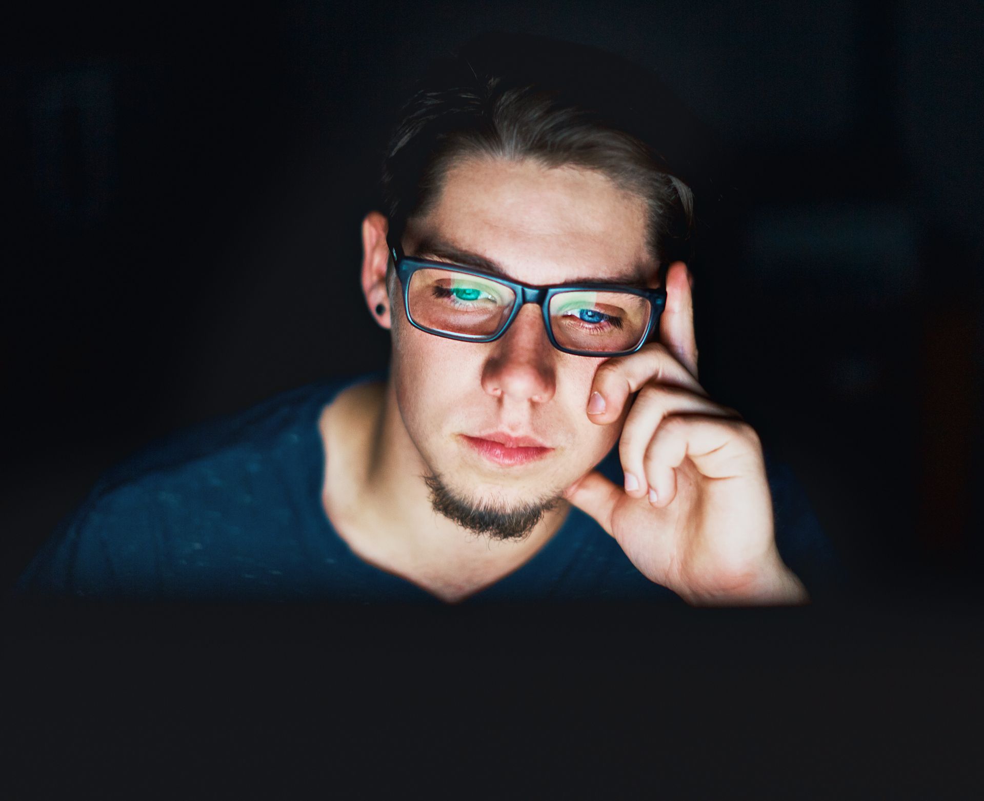Young man sits in the dark staring at computer monitor