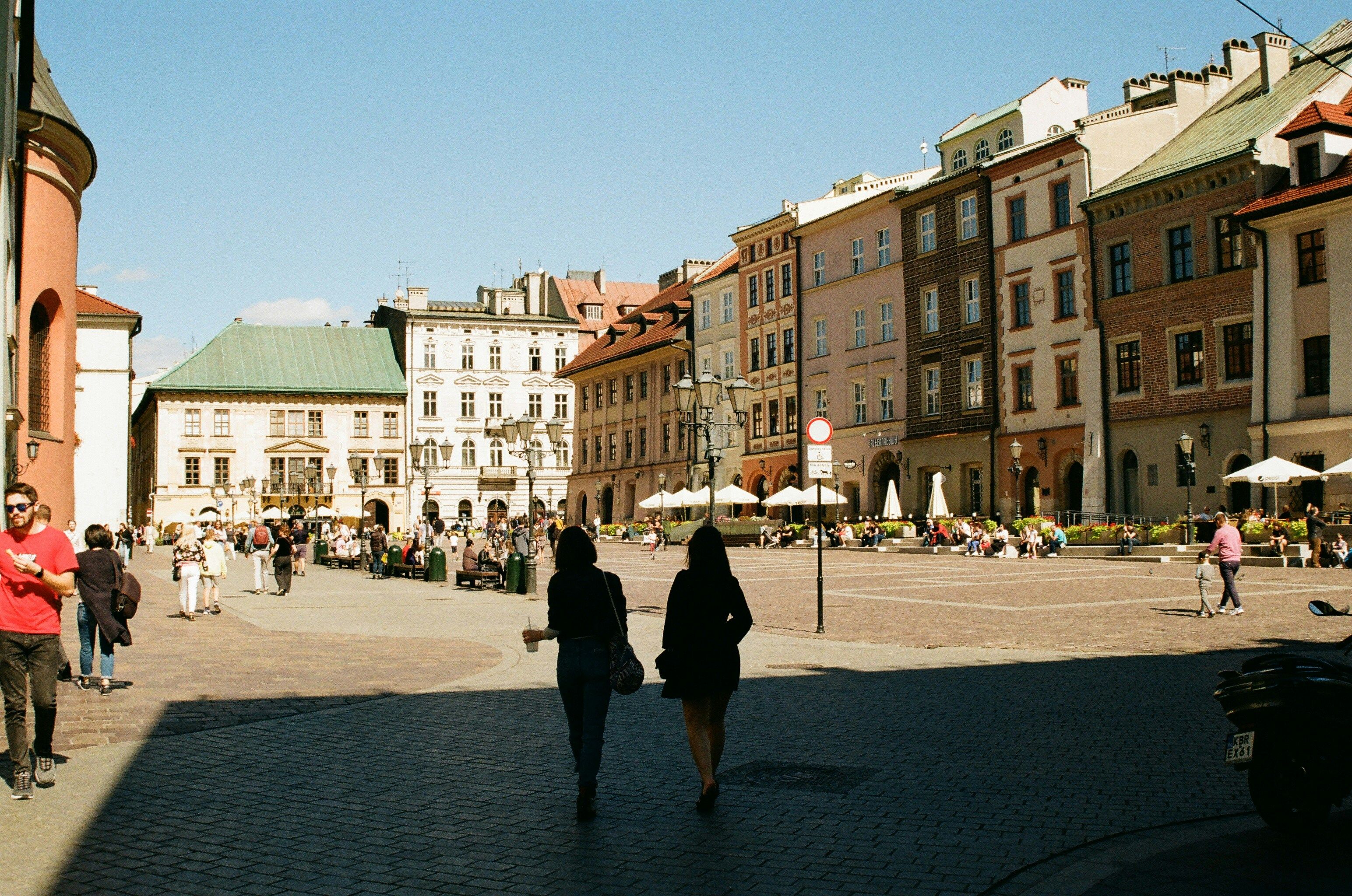 A shadow of two people enjoying a drink walking through an old European town square surrounded by old buildings.