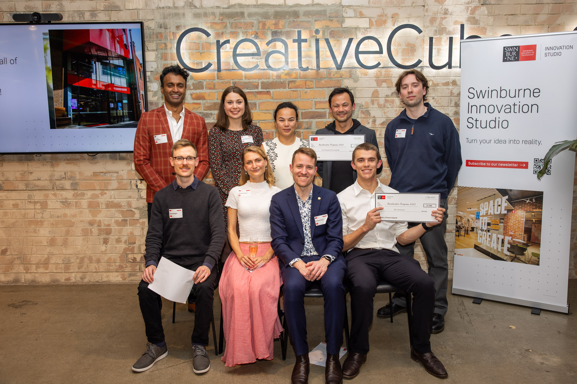 Members of the Five startups at 2023 Swinburne Accelerator Program Demo Night. There a nine people in total, four sitting in from of five people standing. Everyone is smiling at the camera and a few are holding up award certificates