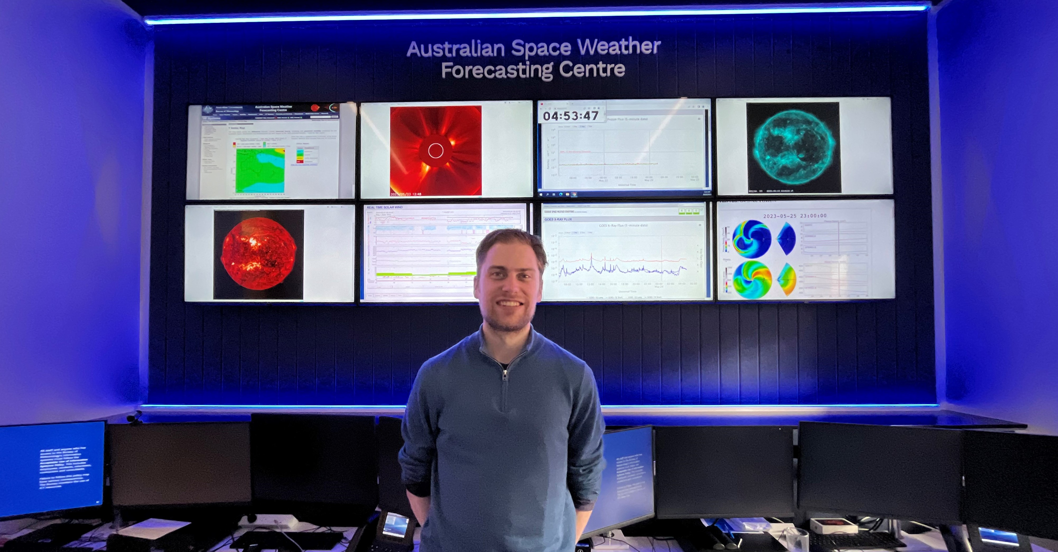 Andrew Jackling at the Australian Space Weather Forecasting centre standing infront of his work station with various monitors showing space weather data