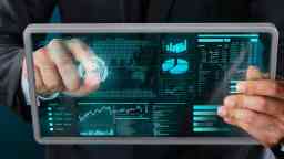 A man in a suit holds a transparent tablet displaying graphs and figures