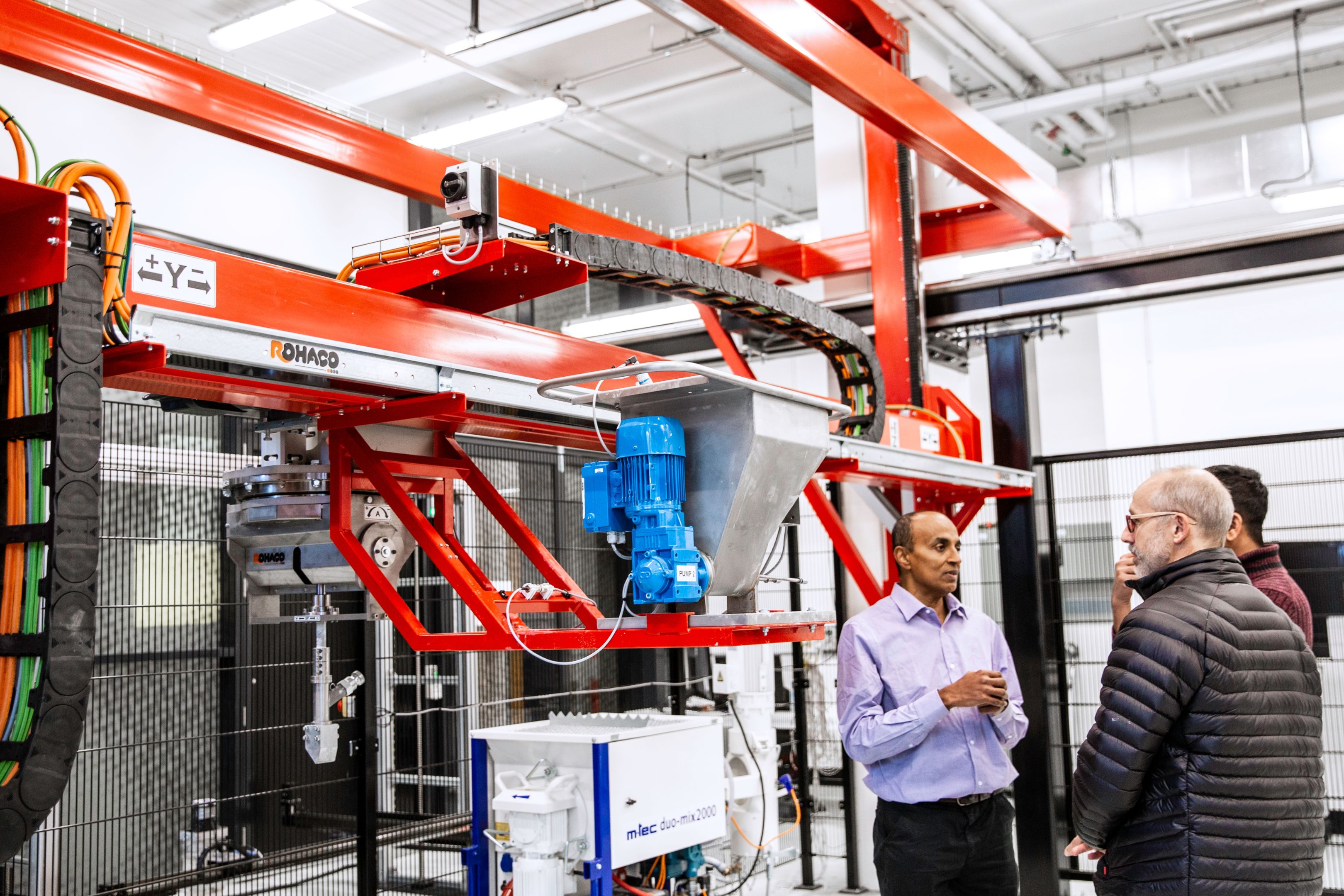 Man showcases machinery from the digital construction lab to two onlookers.