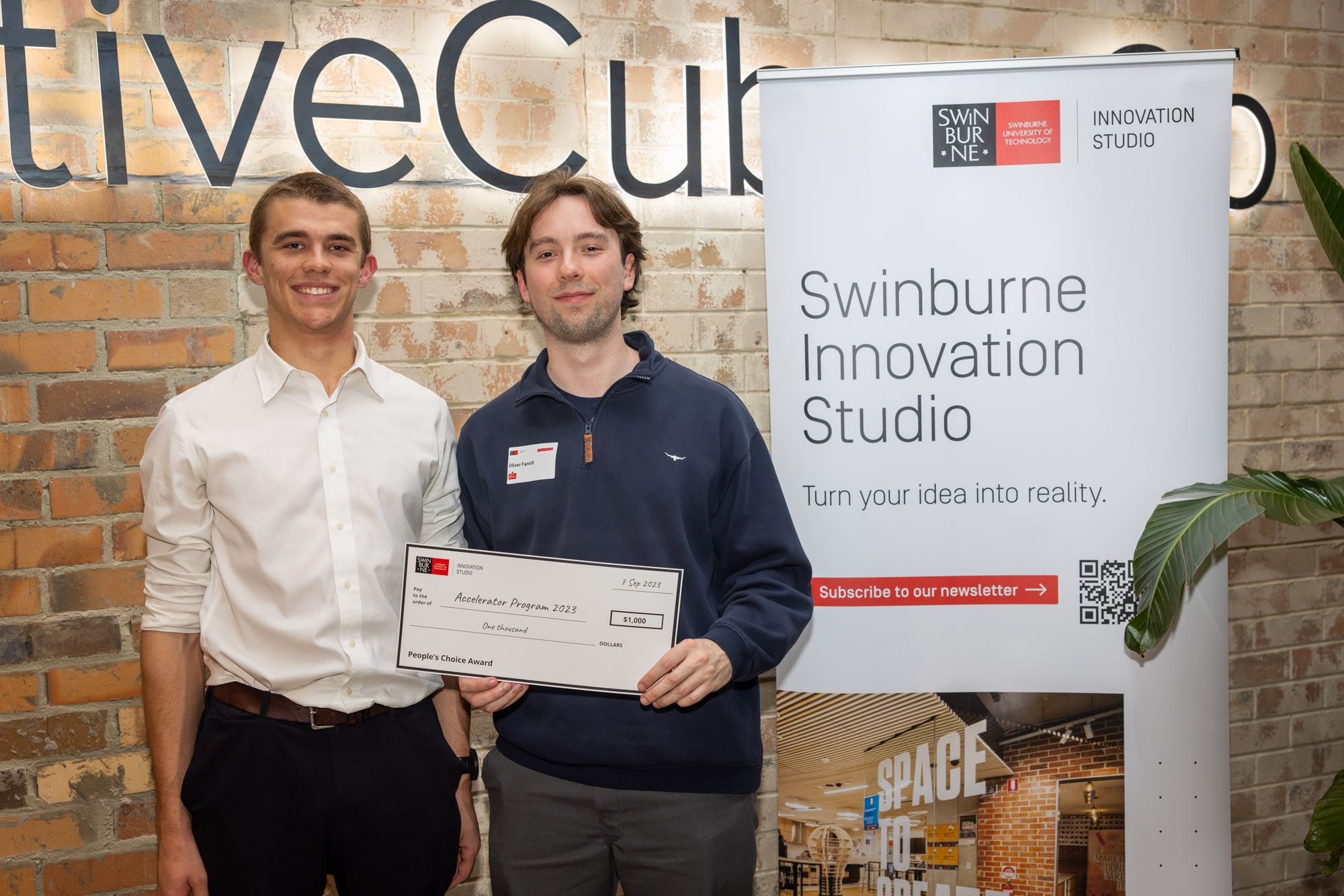 (Left to right) Finnlay Morcombe and Oliver Farnill stand togetehr smiling holding up the People’s Choice award at the 2023 Swinburne Accelerator Program Demo Night.  