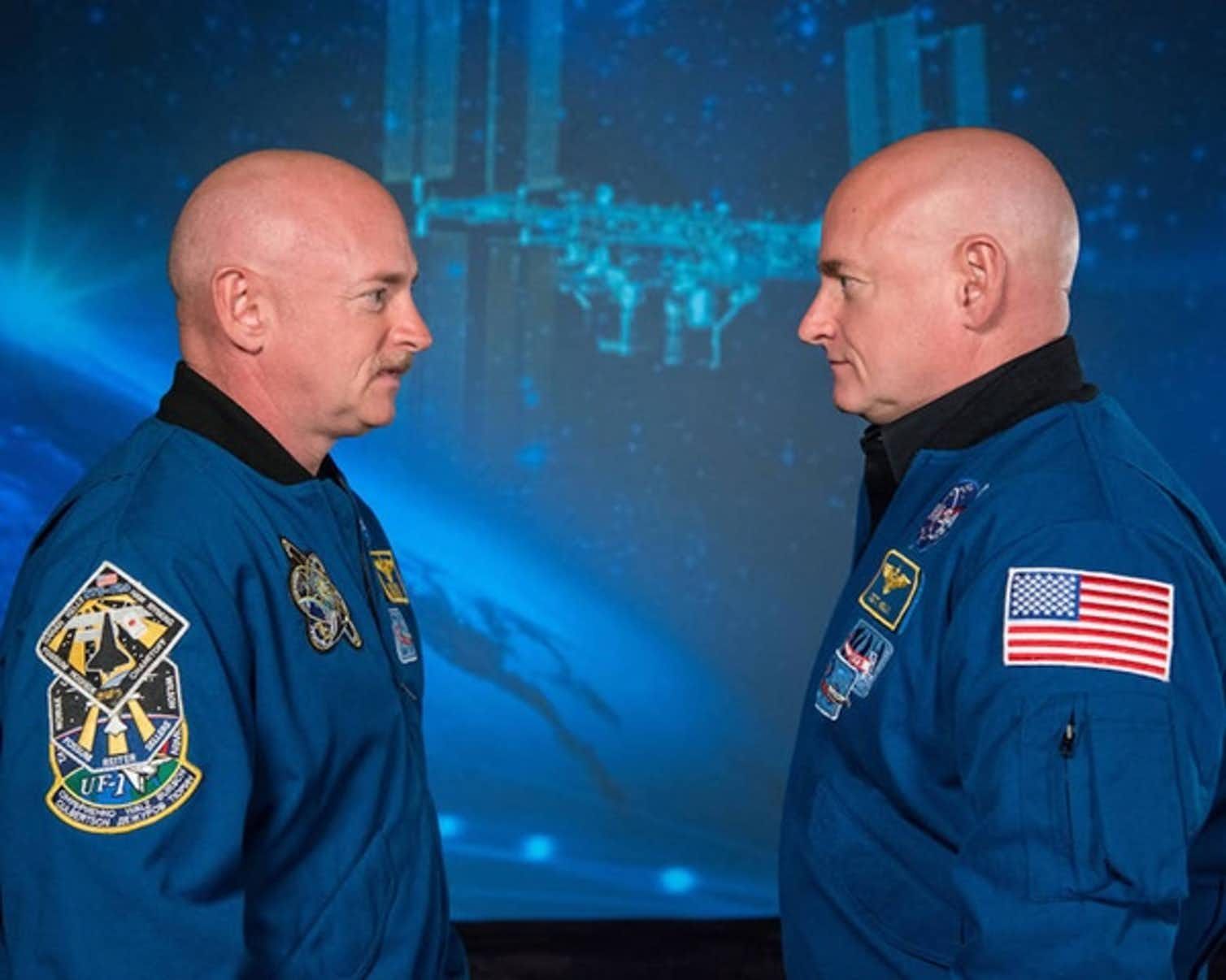 Twins Mark and Scott Kelly standing side on towards each other to exhibit the effects of time in space