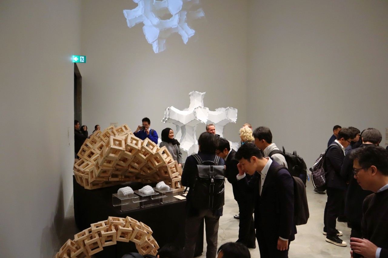 People fill a large room, looking at abstract architectural exhibits