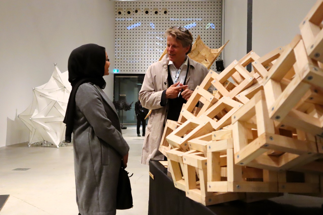 Two people stand discussing a large modular wooden prototype