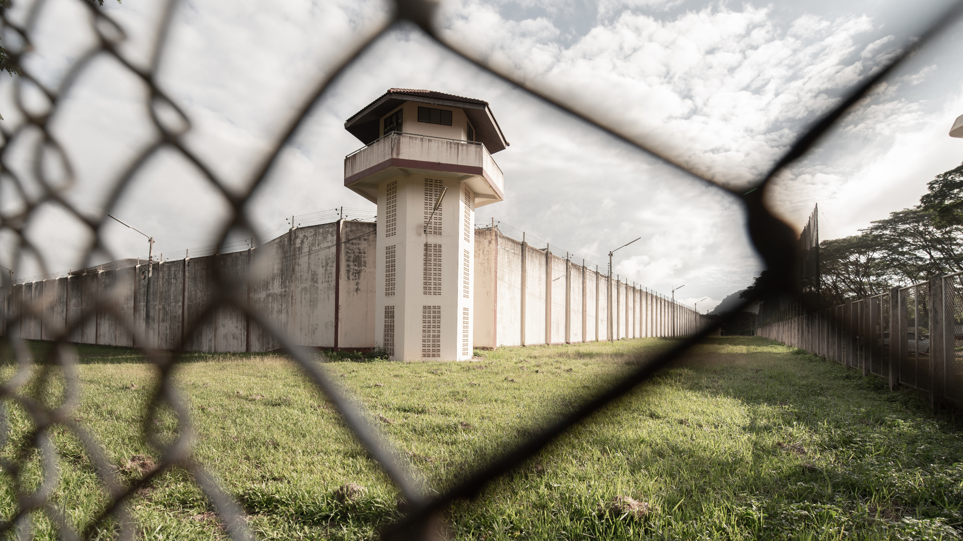 Exterior of a prison surrounded by green grass behind wire fence