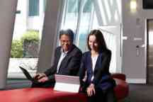 An Asian man and caucasian female in suits looking a laptops in an office setting