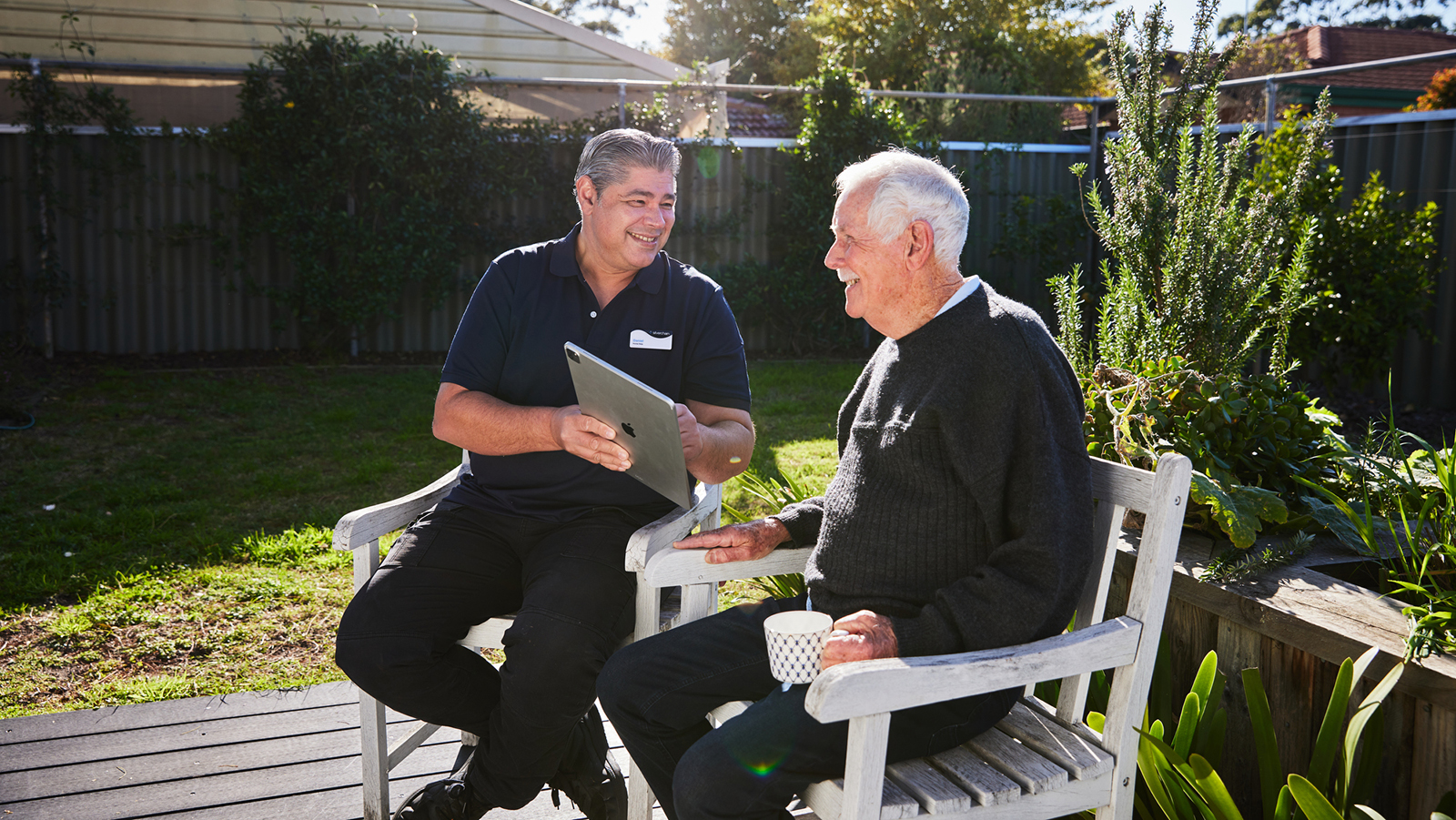 Two men sitting in backyard looking at tablet device