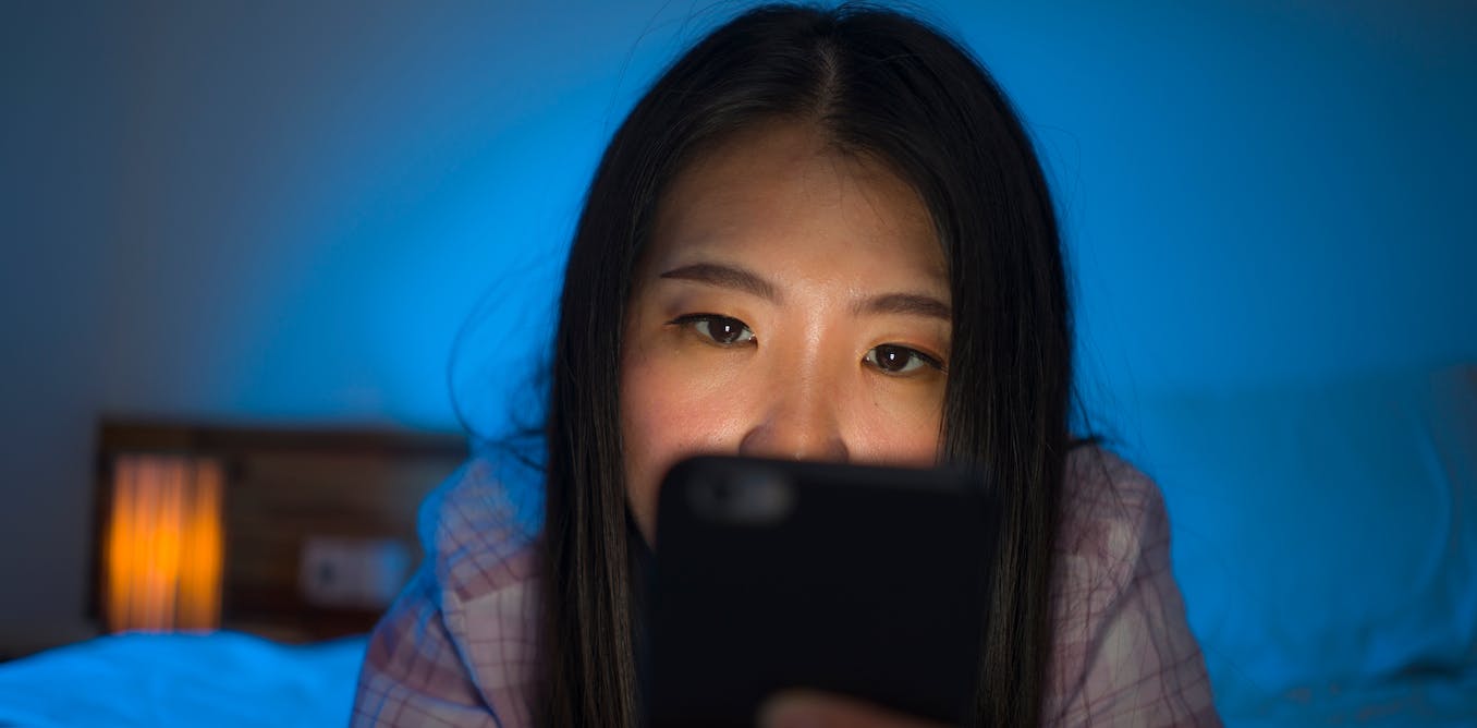 Women looking at her phone whilst laying on a bed 
