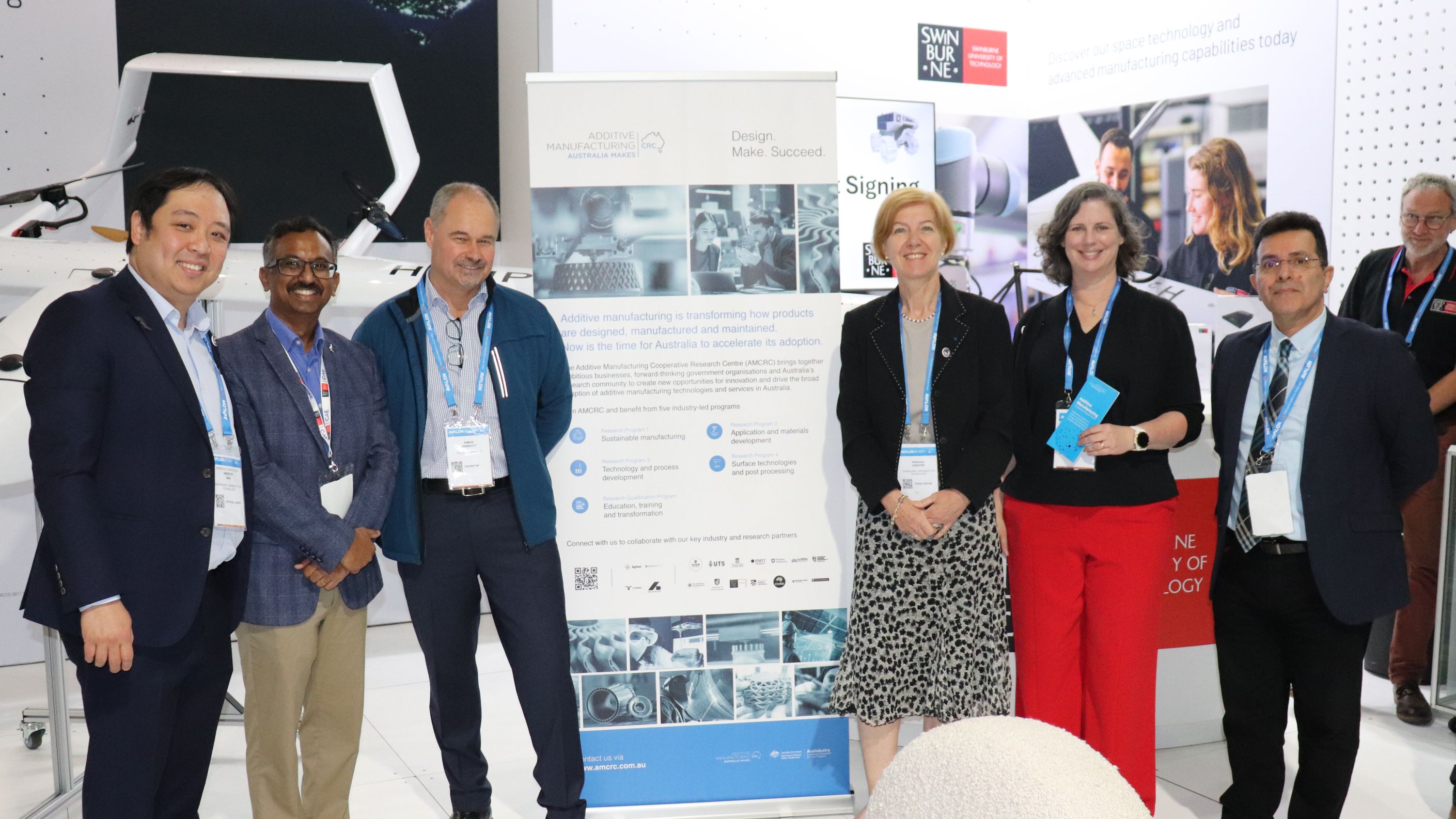 A group of six Swinburne leaders involved in the Additive Manufacturing Cooperative Research Centre stand next to a banner at the Avalon Airshow 2025.