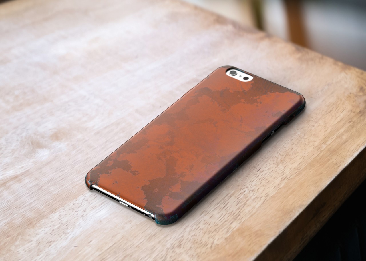 A mockup of a copper phone case sitting on a wooden table, medium-heavy wear and darkening