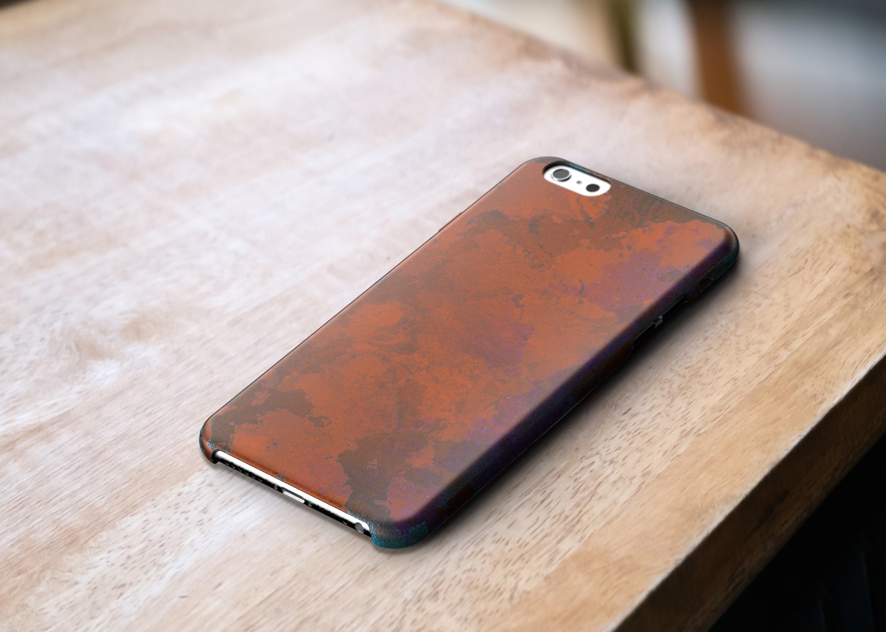 A mockup of a copper phone case sitting on a wooden table, heavy wear and darkening