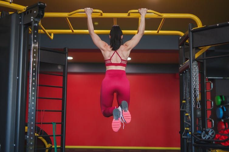 Women with her back turned performing a dead hang in the gym
