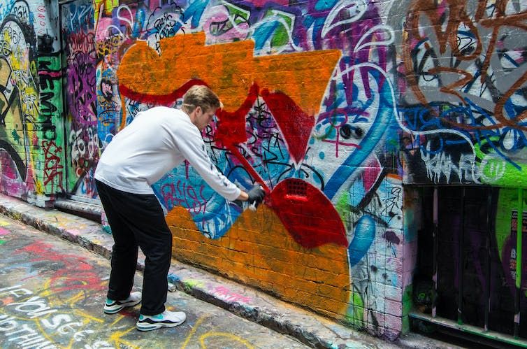 Man using a spray can to create graffiti art in a Melbourne alleyway