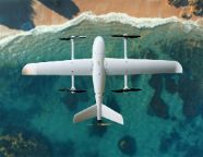 A white uncrewed drone flies above water and a beach