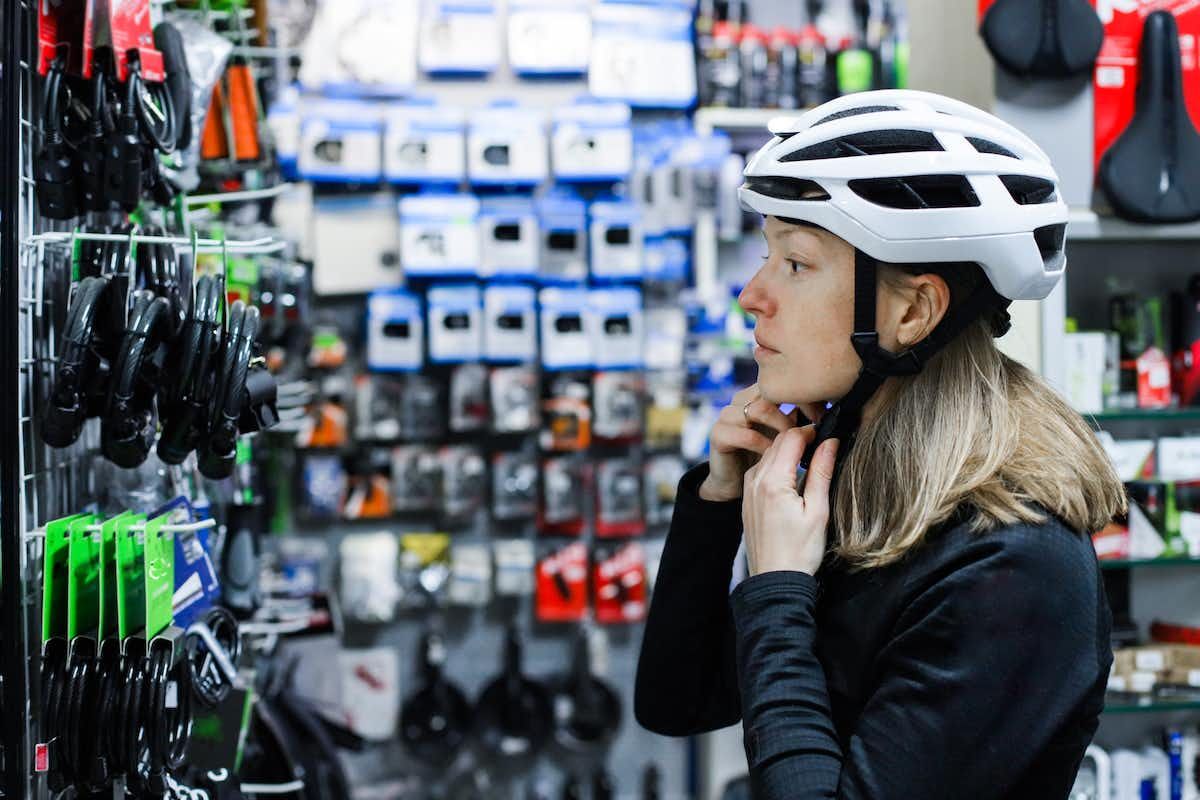 A woman trying on a white bicycle helmet in a bike store.