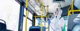 Public transportation healthcare. Man in white protection suit disinfecting and sanitizing handlebars and bus interior to stop spreading highly contagious coronavirus or COVID-19.