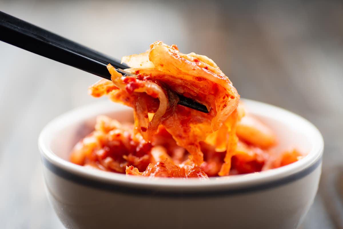Close-up of Kimchi in a small bowl being picked up by chopsticks.