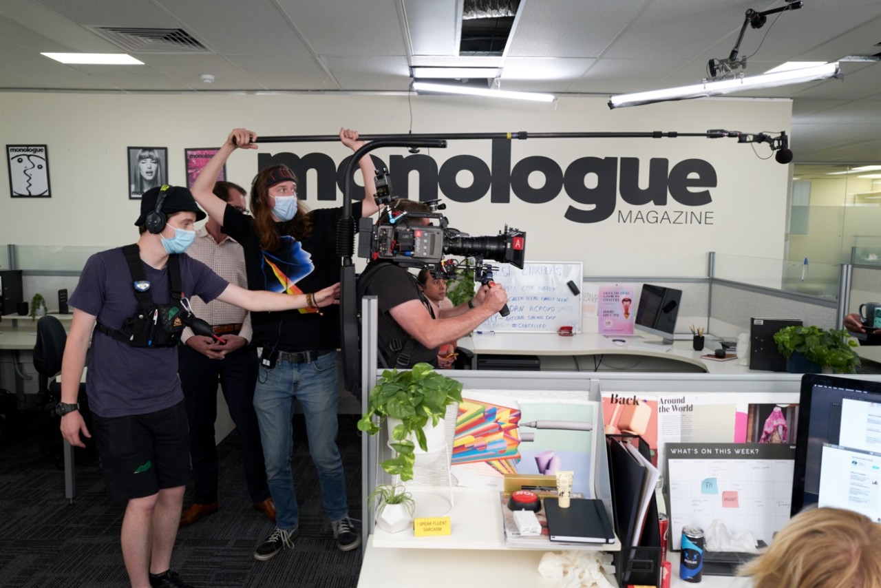 Students filming the satirical mini series, Monologue - in an office space with a camera, boom mic and camera guide