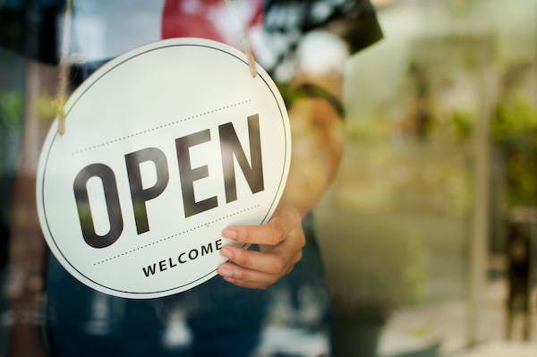 A person turning around the sign on the front of their business to read 'open welcome'