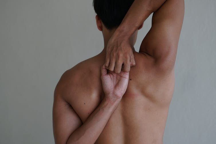 Man with his hands behind his back, performing a shoulder stretch 