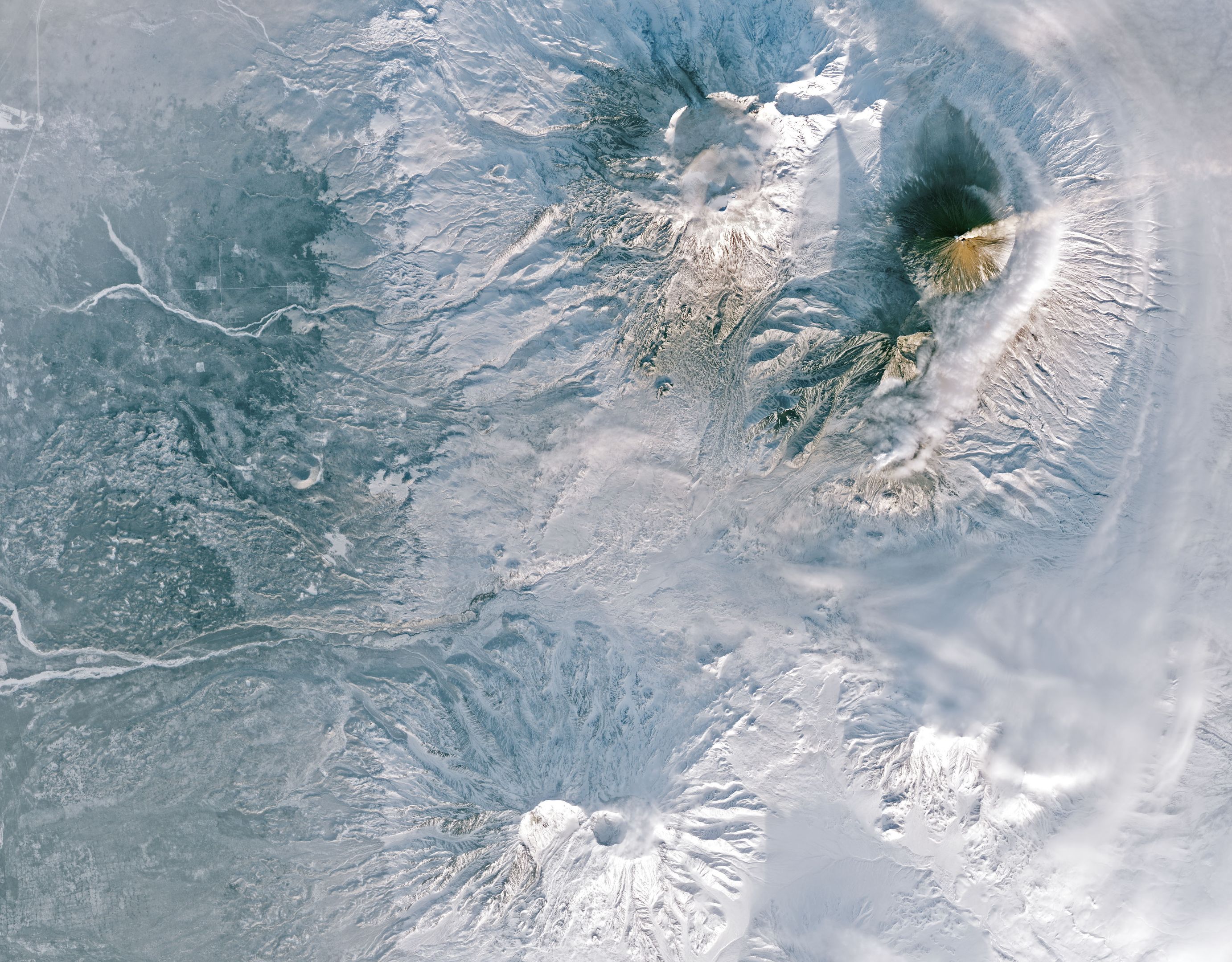 A birds-eye view of an active volcano smoking, surrounded by a snowy landscape.
