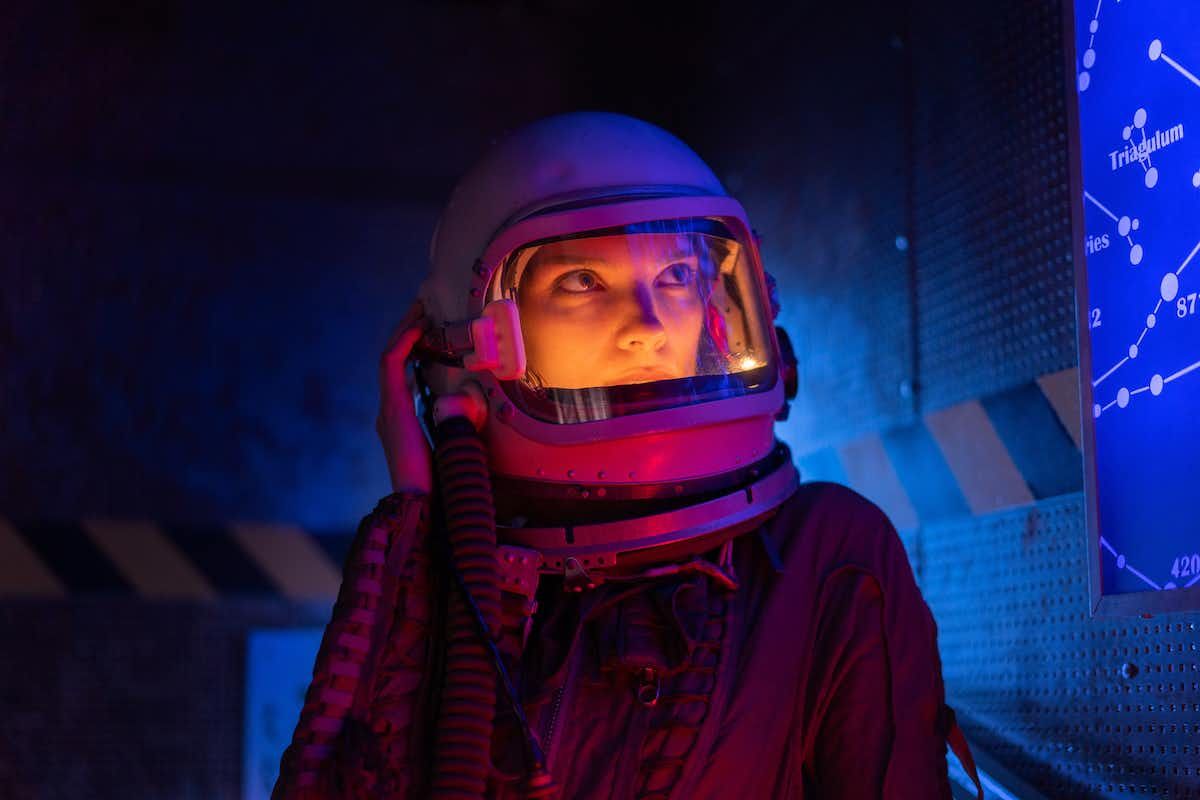 A woman wearing an astronaut suit under some blue and pinking lighting