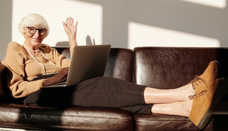 Woman waving as she sits on a couch with a laptop